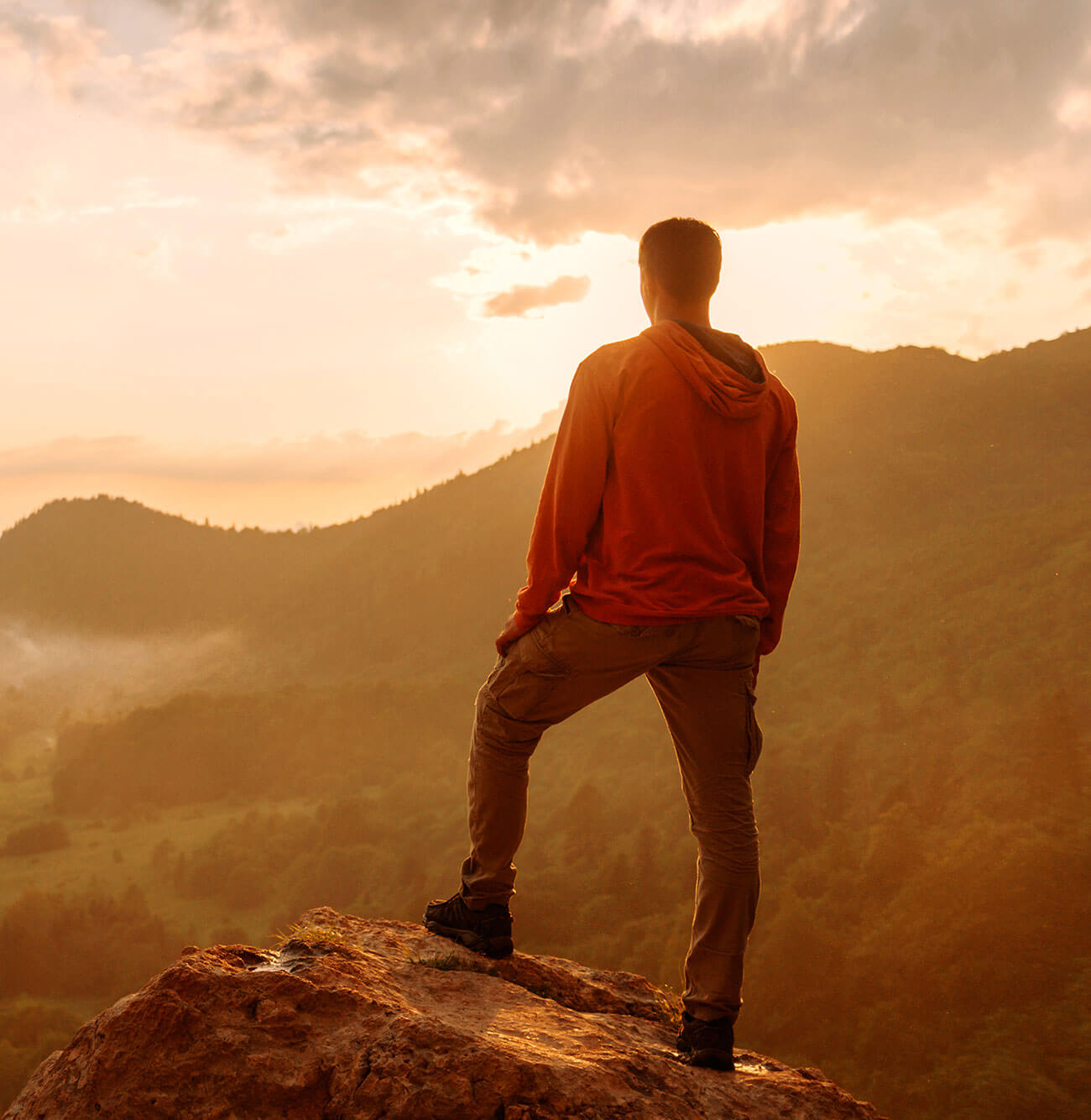 Man standing at sunrise on a mountain peak.